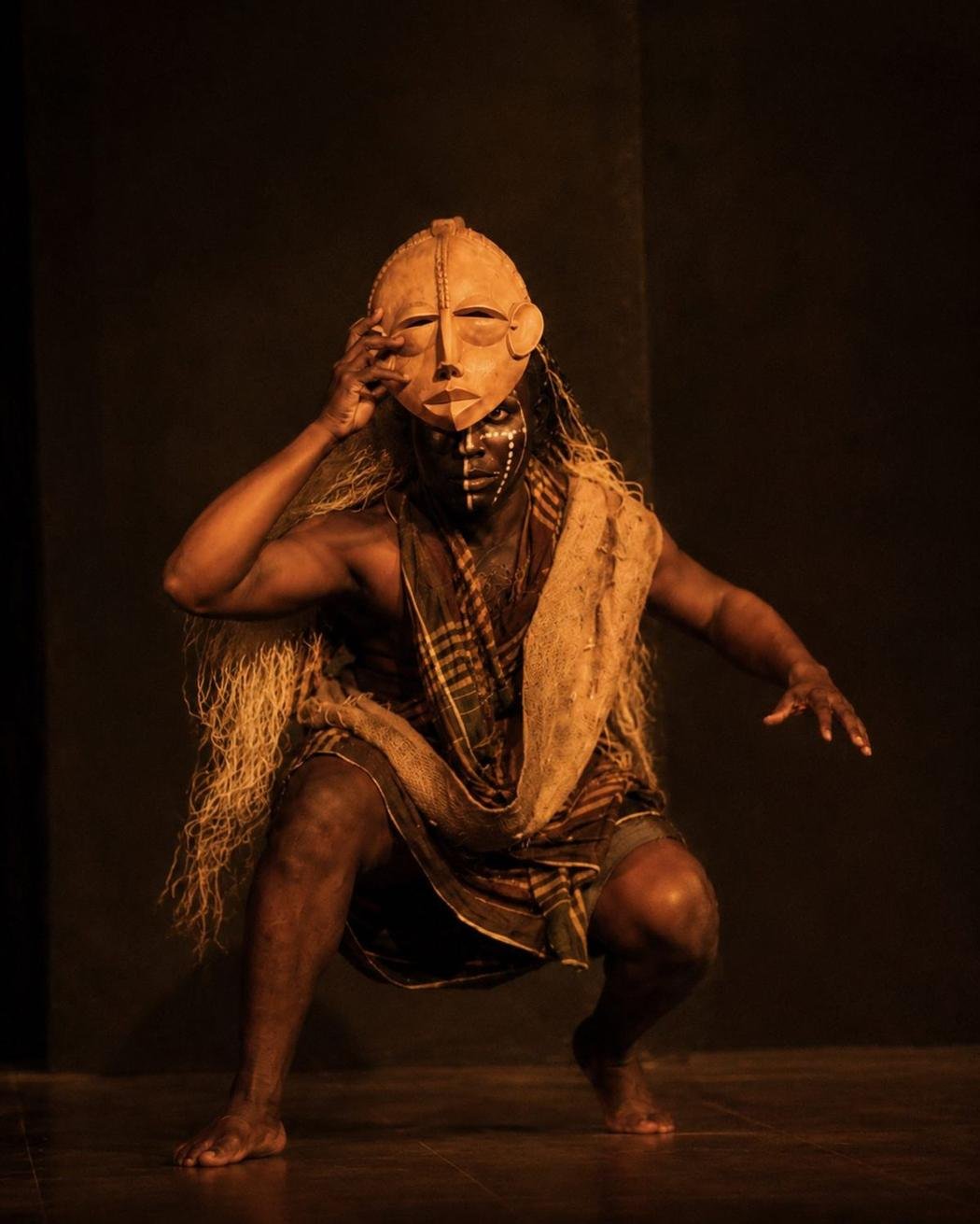 A masked performer lifting the mask from their face
